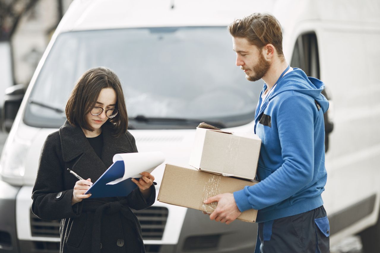 Mastering the First Impression: Your intriguing post title goes here A courier in blue hands packages to a woman signing documents in front of a delivery van.